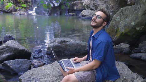 Man-working-with-laptop-at-waterfall.